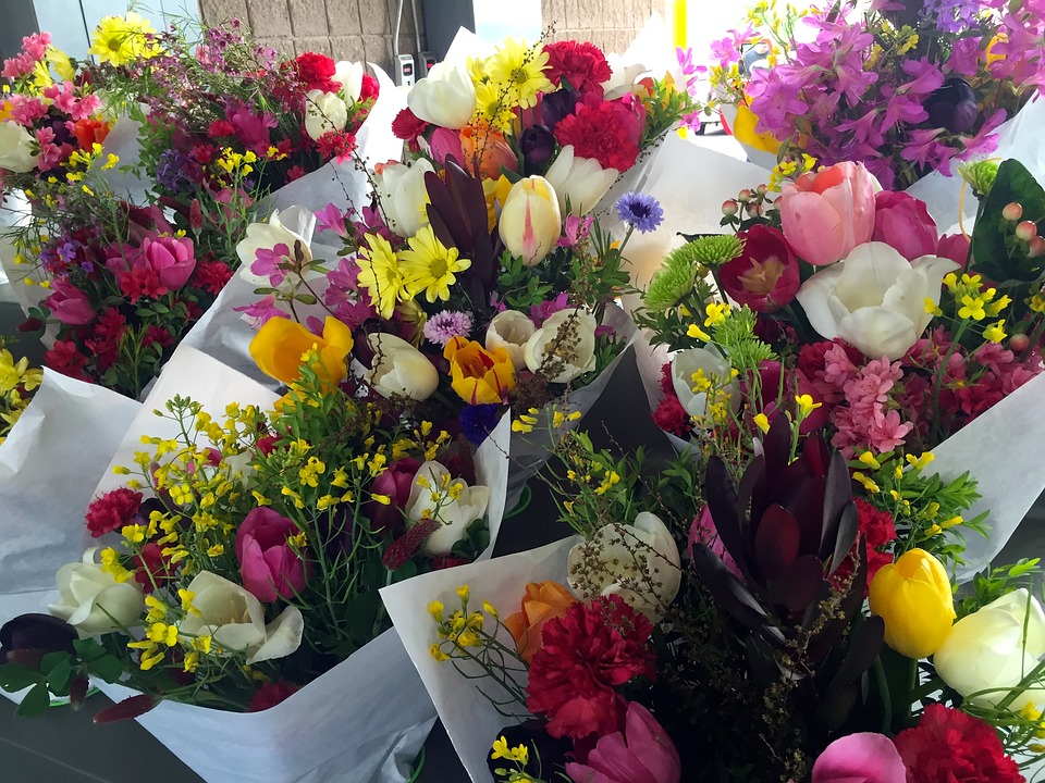 Vivid picture of 9 bouquets of fresh flowers, yellow, pink, orange, purple, white green in color, neatly packed in white paper