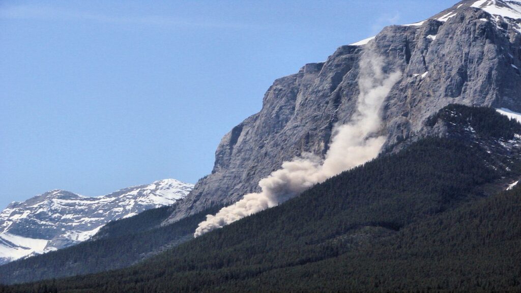 Smoky landslides on grey slope with vegetation in foreground and snow capped mountain at the back, on Alberta mountain, Rocky mountain chains in Canada