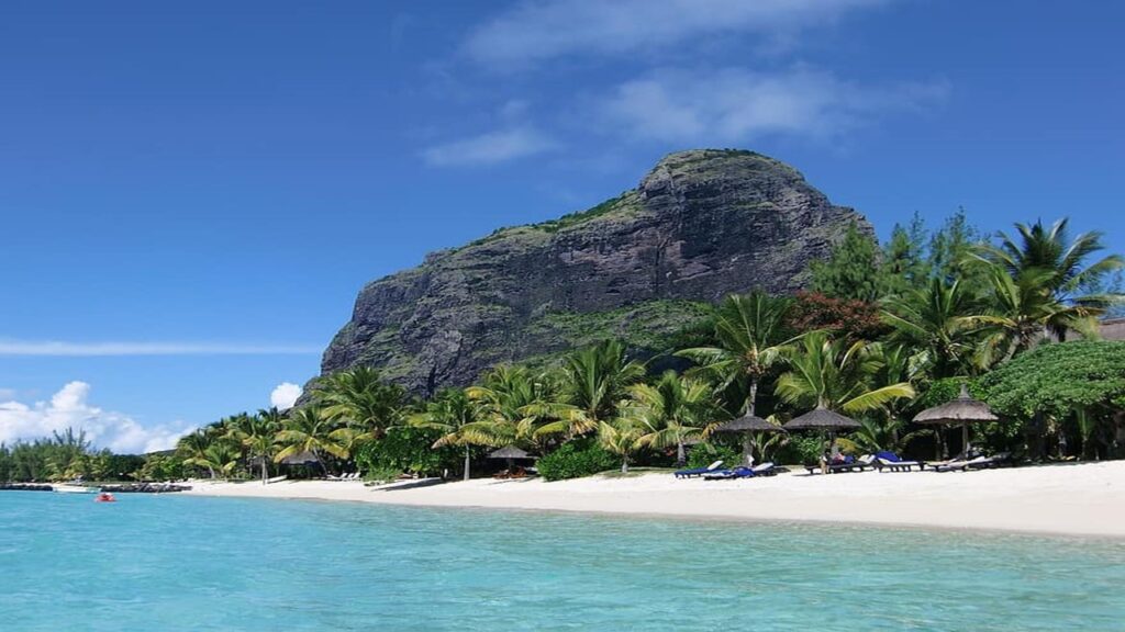 grey mountain backdrop with coconut trees, white beach and sun chairs in front of the sea, Le Morne Mauritius underwater waterfall