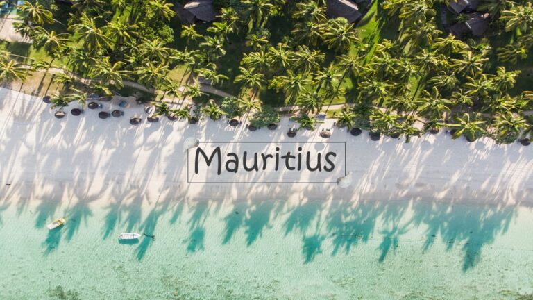 Mauritius Island: turquoise blue waters with two small red boats, white beach with Mauritius written in black box and green palm forest at the back: Geography, history, travel and weather; sustainable tourism