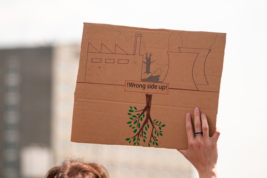 Hand holding brown paper with industries on top and tree at the bottom, sign reading wrong side up, environmental studies