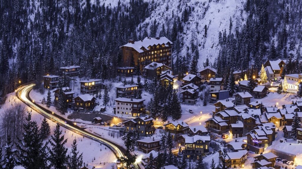 Courchevel town in France with small lighted wooden chalets and lighted road covered in white snow