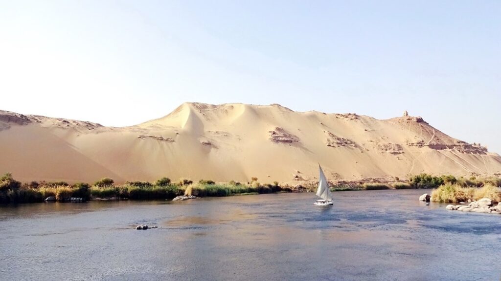 white boat sailing in water of nile basin with white sand dune on the coast
