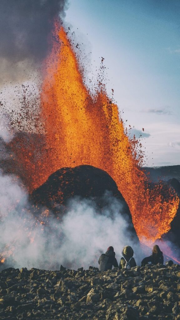 Volcanic eruption of the Fagradalsfjall, Iceland, with orange lava spurting into the air and three people watching